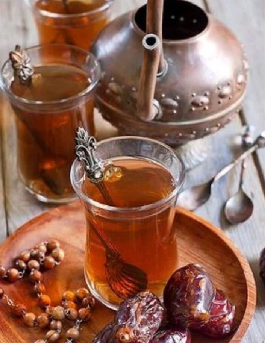Arabic tea tradition — glasses of tea with dates and prayer beads beside a traditional copper dallah pot